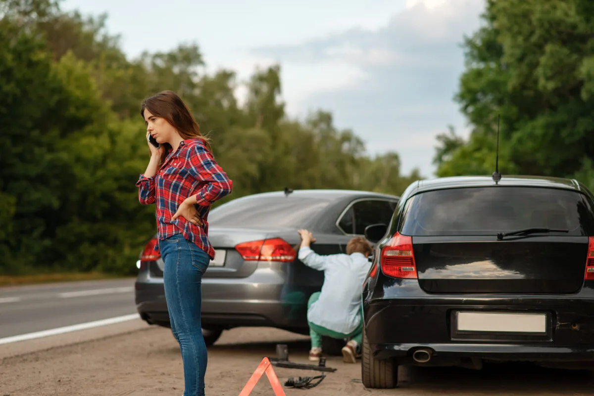 a woman on the phone next to a man looking at a broken car